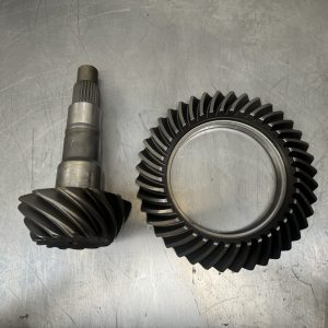 The NEW Holden Salisbury 10 Bolt Ring & Pinion set is displayed side by side on a scratched metal surface, highlighting their helical teeth and precision-machined finishes.