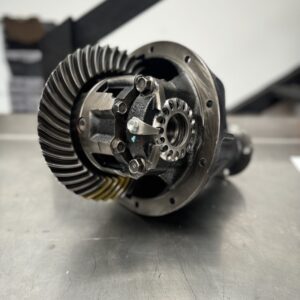 A close-up of Import placeholder for 1840, a metal mechanical differential gear component, placed on a metal surface with detailed gears and bolts visible in a workshop setting.